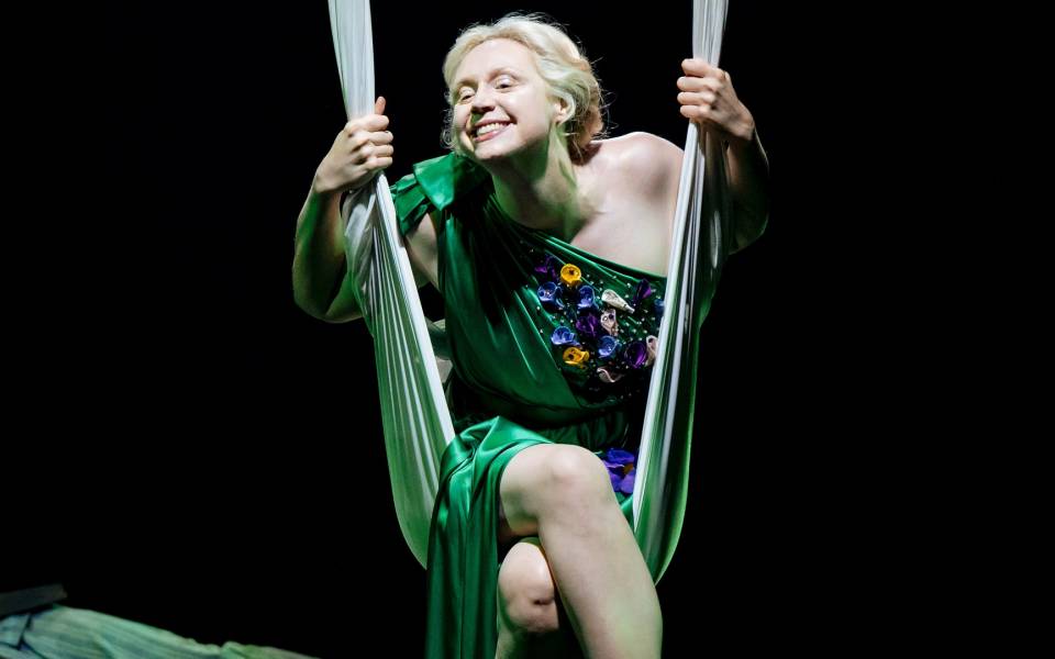 Gwendoline Christie (Titania) swings on a length of silk, with a cheeky grin
