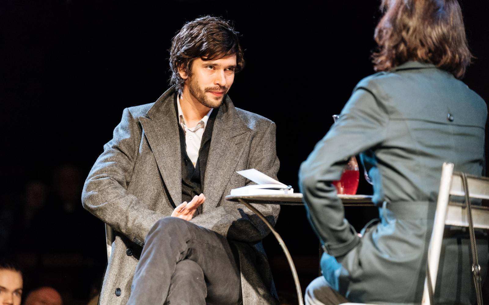A man and a woman, dressed in outdoor clothes, sit at a table and talk
