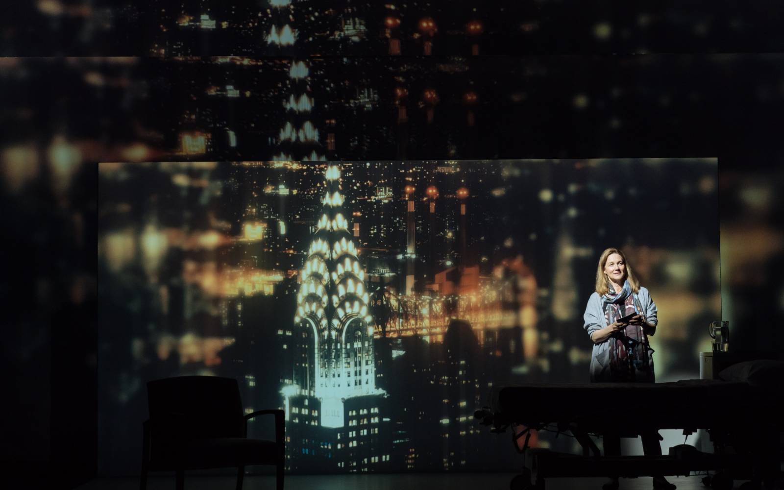 Laura Linney gazes wistfully out of frame, standing in front of a projection of the New York City skyline at night