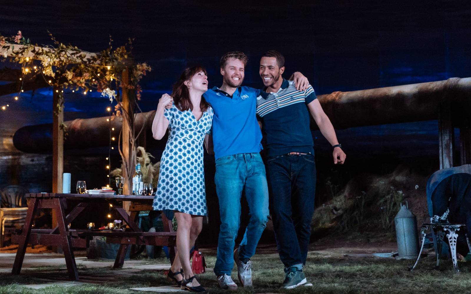 Three young adults look giddy, arms around each other, standing under the night sky