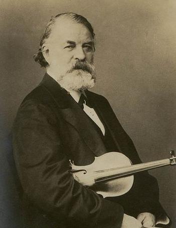19th-century photograph of a man with a bushy, grey beard, holding a violin under his arm.