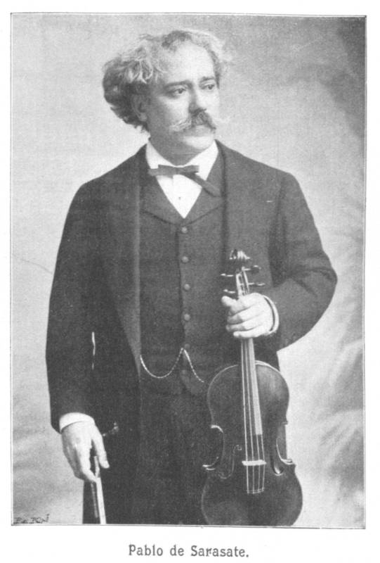 19th-century photograph of a man with grey, curly hair, standing up and holding a violin in one hand.